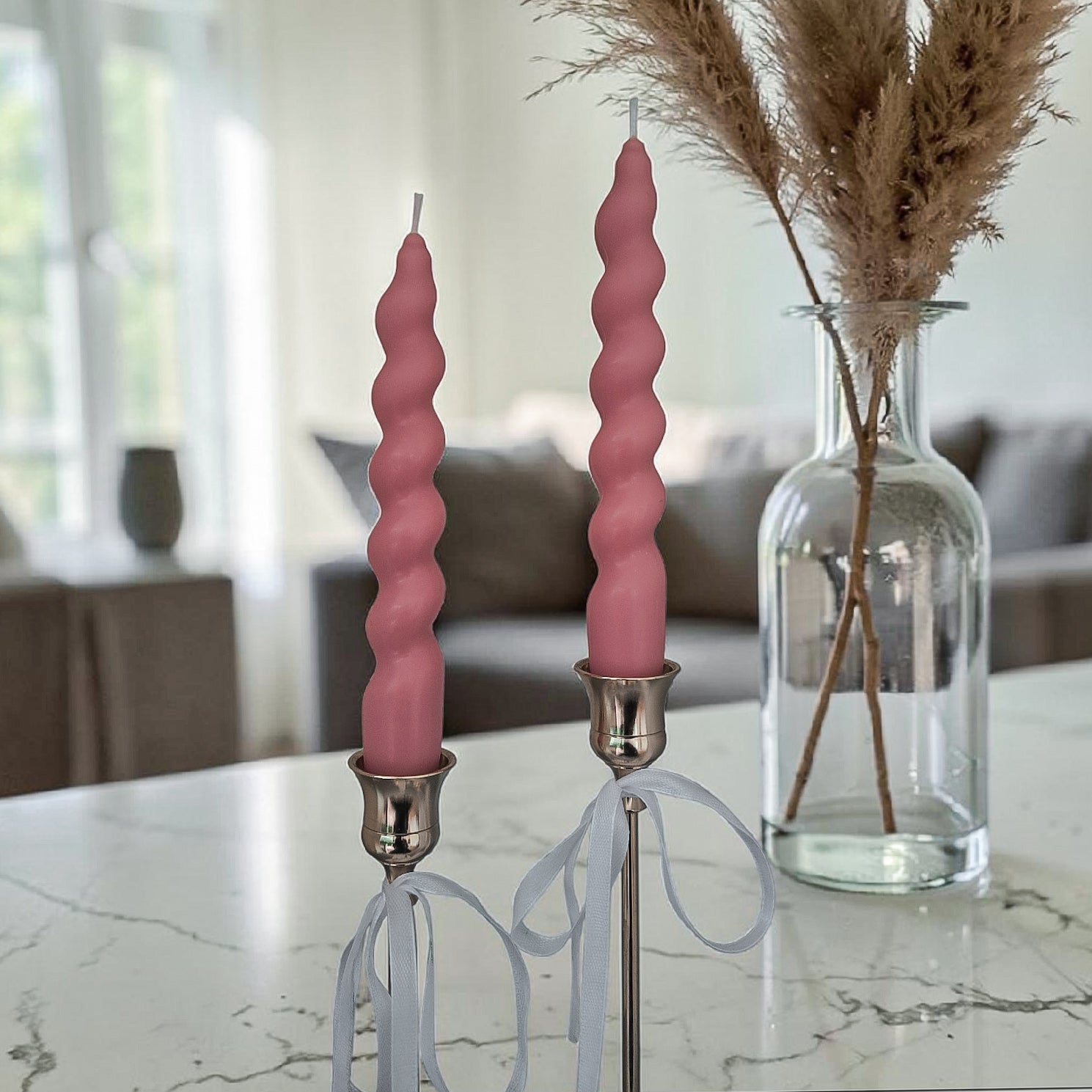 Hand poured soy wax pink spiral candles in silver holders on a marble surface with a blurred indoor background