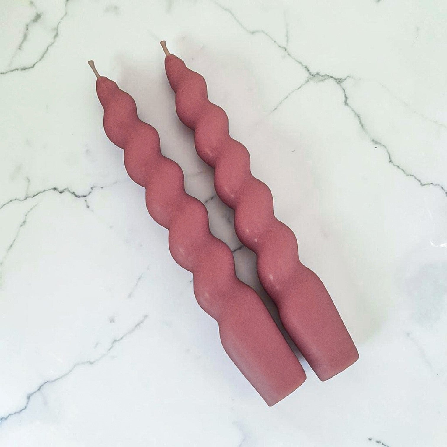 Two hand poured soy wax twisted pink candles on a marble surface