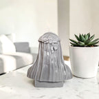 Hand poured soy wax decorative candle with a veil and bow on a marble surface next to a potted plant.