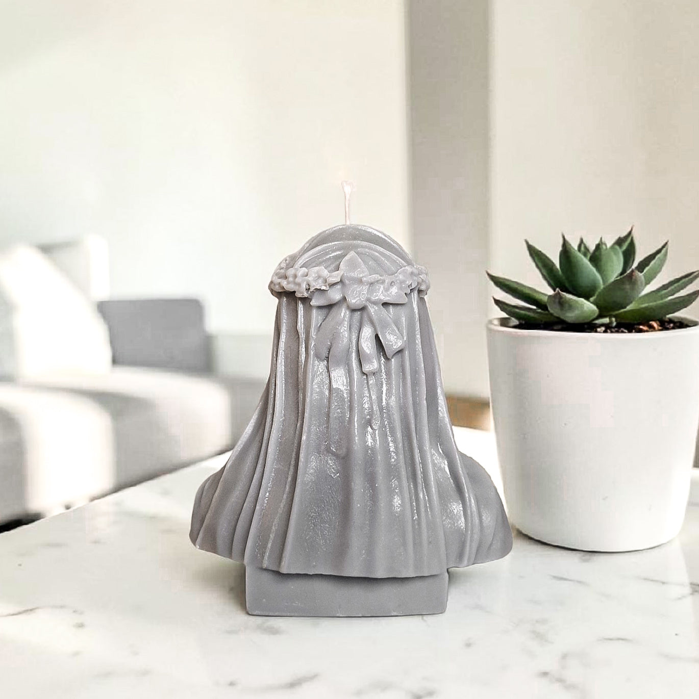 Hand poured soy wax decorative candle with a veil and bow on a marble surface next to a potted plant.