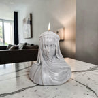 Hand poured soy wax Candle in the shape of a draped figure on a marble surface with a blurred indoor background