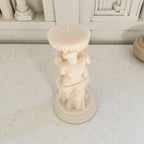 Candle in a statue-shaped holder on a light surface