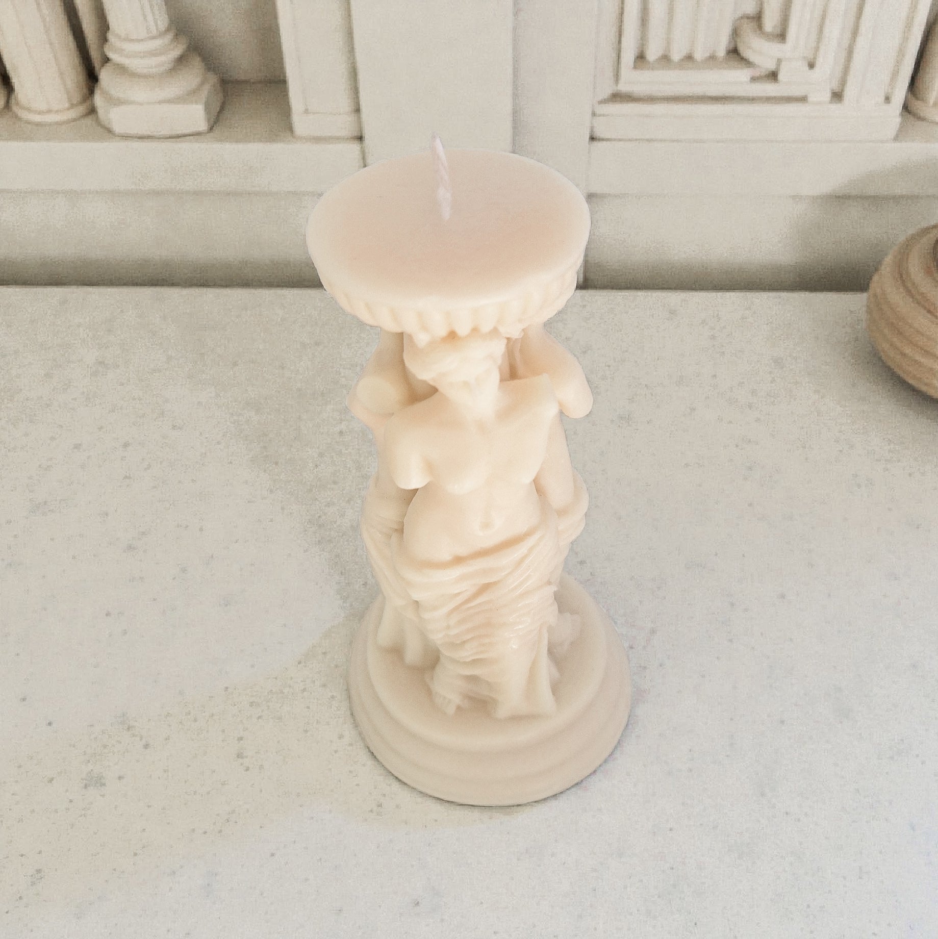 Candle in a statue-shaped holder on a light surface