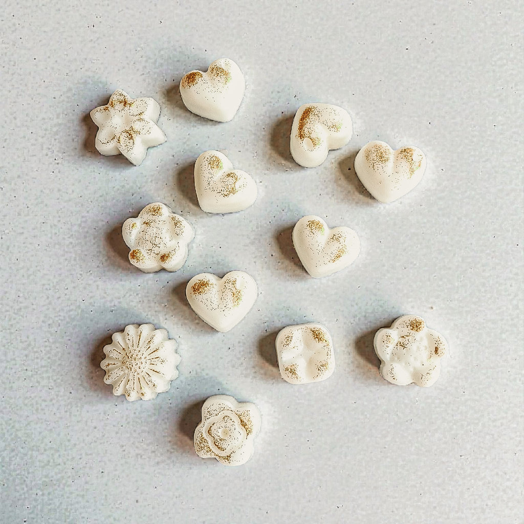 White soy wax melts in star and heart shapes with gold dust on a light grey surface