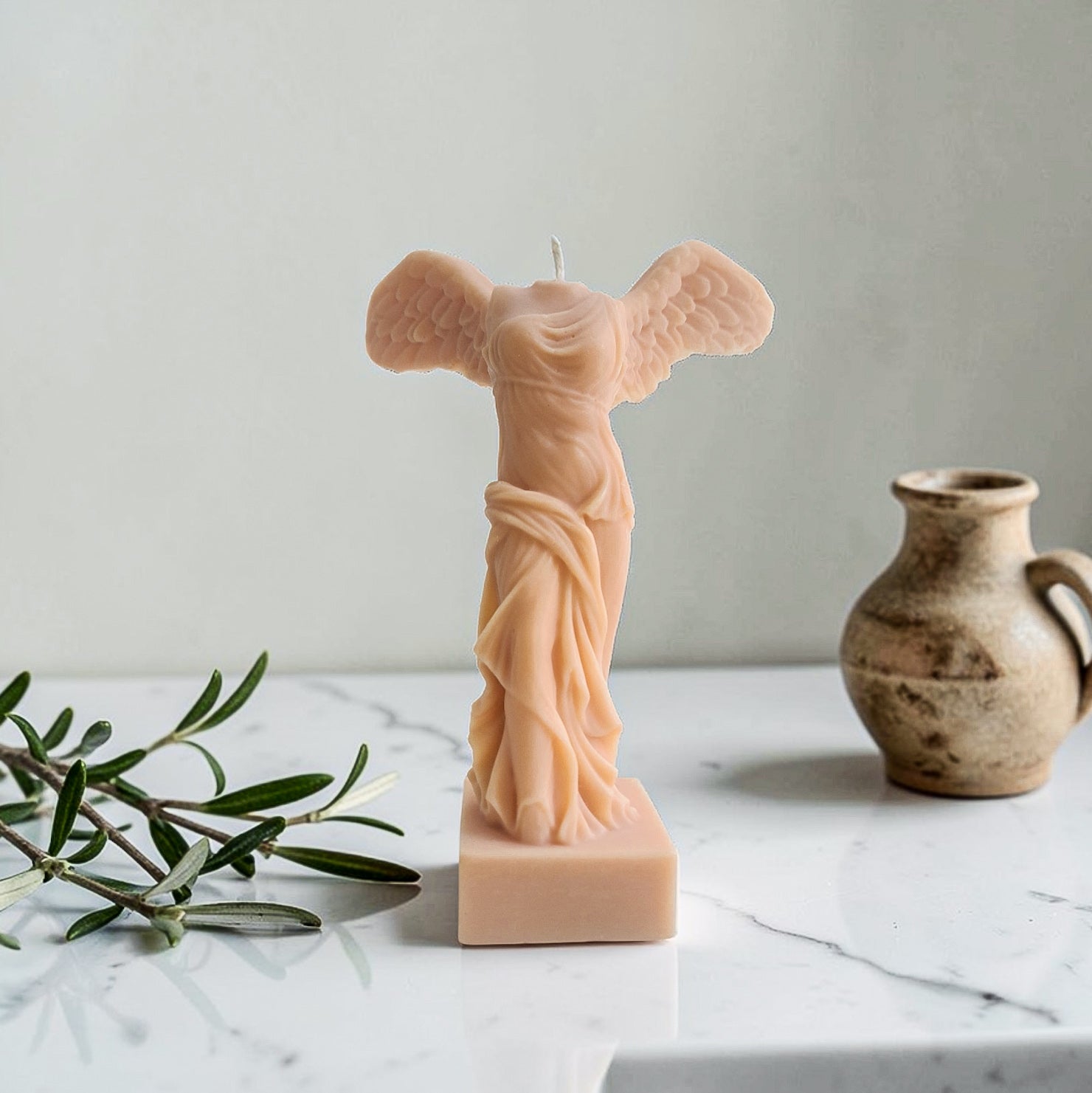 Candle shaped like a classical statue on a marble surface with a vase and olive branch - aka winged victory of Samothrace