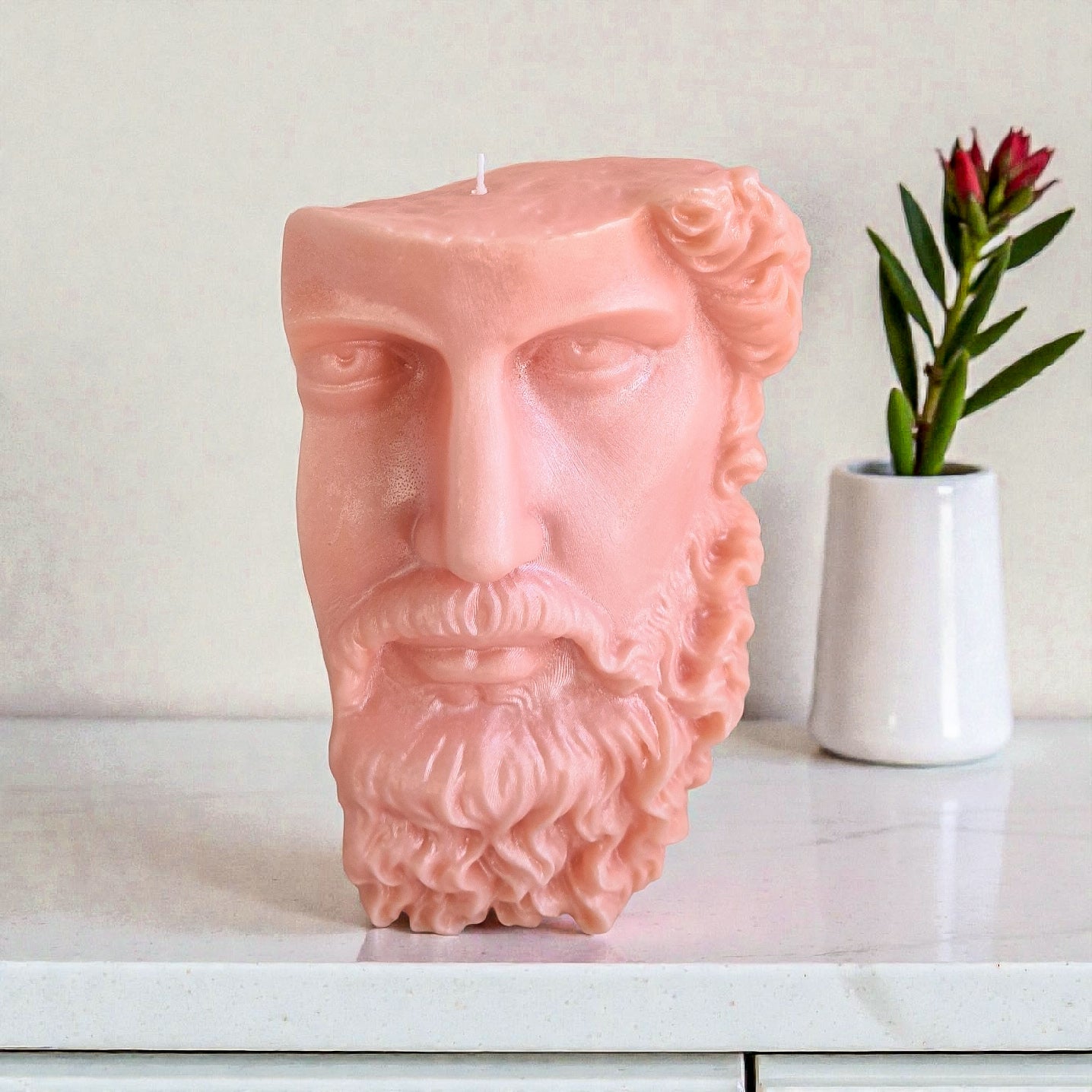 Pink ceramic head sculpture on a white surface with a plant in the background